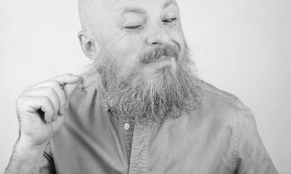 Bald man inspecting his beard hairs for shedding, looking concerned about excessive beard hair loss.