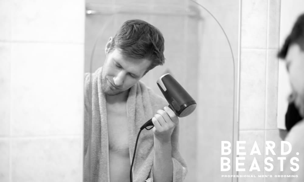 Man using a blow dryer to fix flat hair by lifting it at the roots—part of an effective daily routine for men.