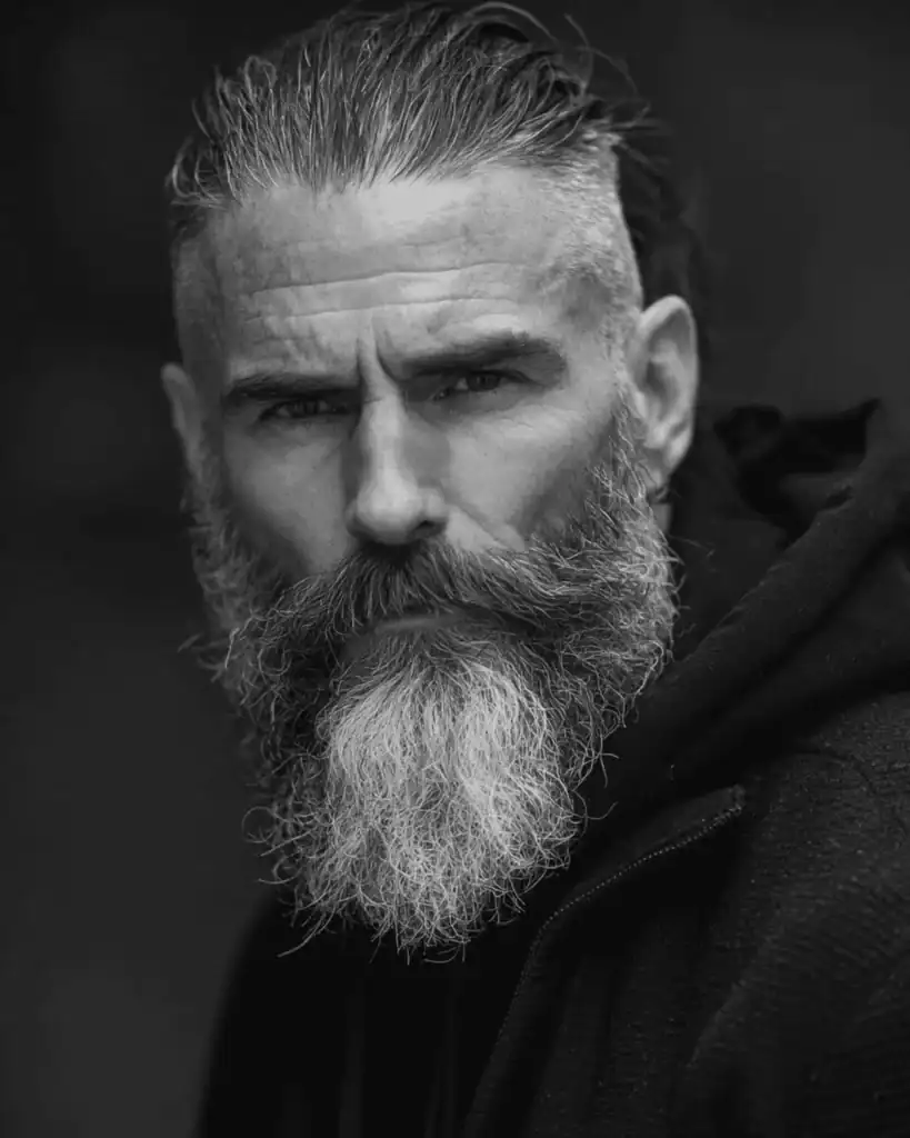 A portrait of a rugged older man sporting a thick full beard with a prominent mustache, showcasing volume and length for a commanding look.