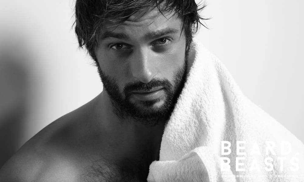 Man with damp hair and a white towel over his shoulder, looking serious—highlighting post-shower grooming mistakes with hair paste.