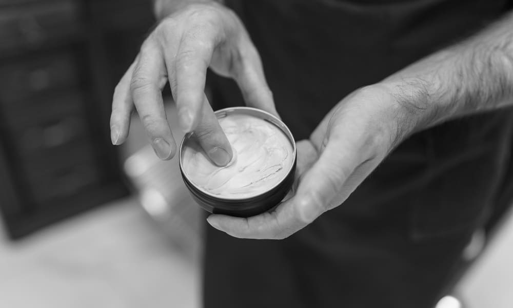 Barber scooping pomade for styling an haircut with a slicked-back disconnected undercut look.