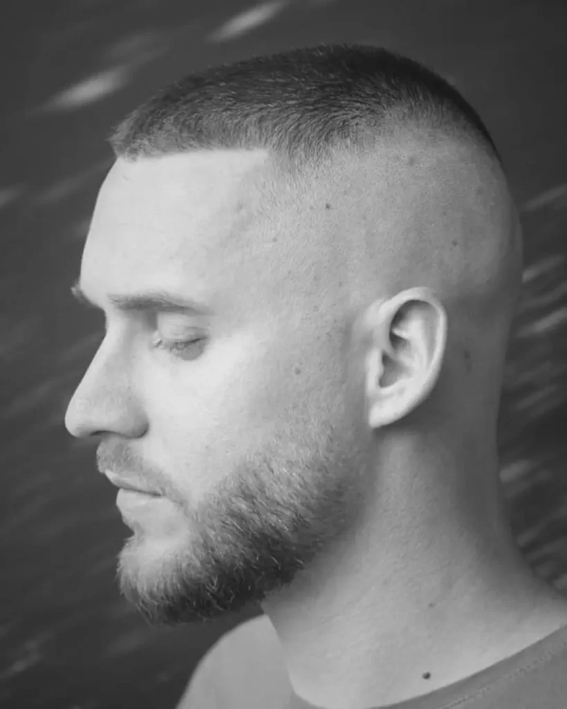 High and tight haircut with a beard, showing very short hair on top with high faded sides and shaped facial hair.