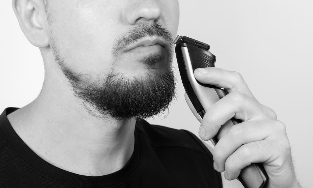 Man using a beard trimmer to shape his mustache at home, demonstrating how to trim your mustache with an electric trimmer.