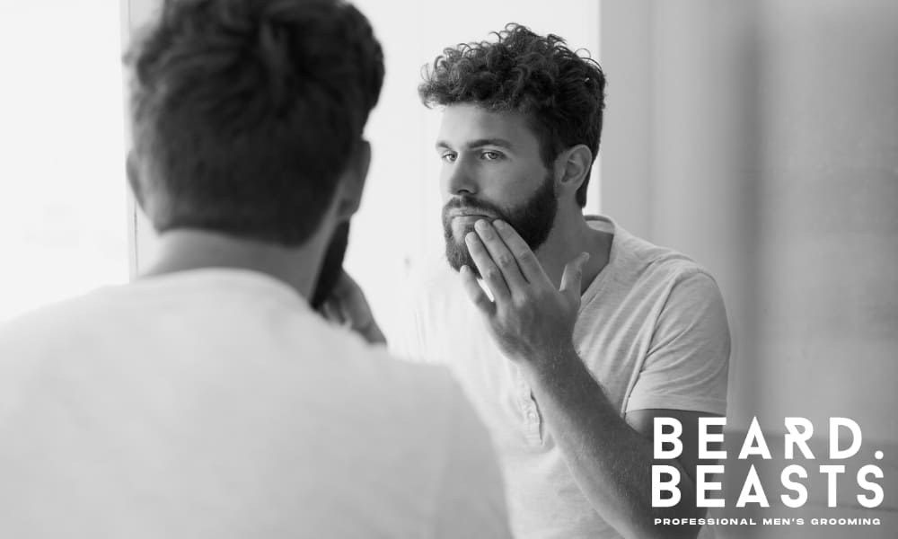 Man examining his beard in the mirror during the day, checking for puffiness or stray hairs as part of his grooming routine
