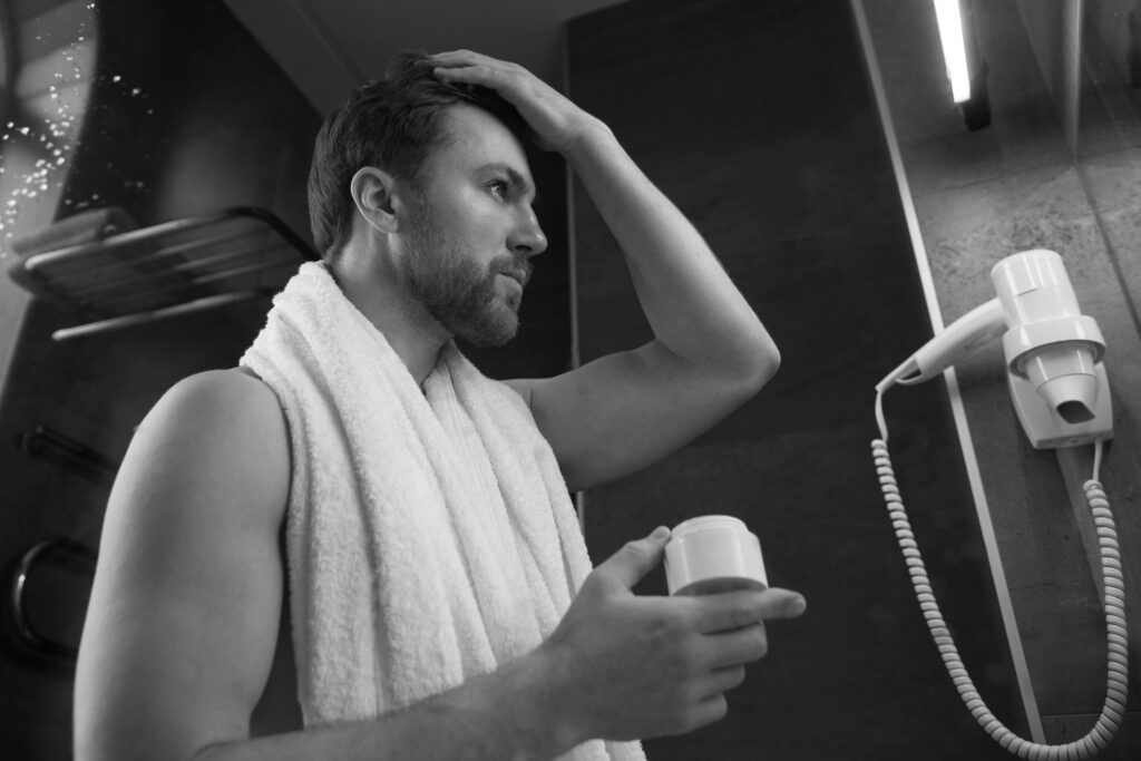 Man applying hair product in front of mirror after shower, representing daily grooming routine for best men’s hair products