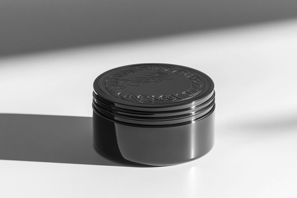 Dark green tin of men’s hair pomade with embossed lid, photographed in natural light on a white surface—premium hair styling product packaging