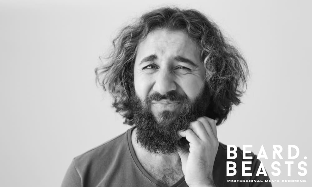Confused man scratching his curly beard with a doubtful expression—illustrating common grooming mistakes and frustration with beard care.