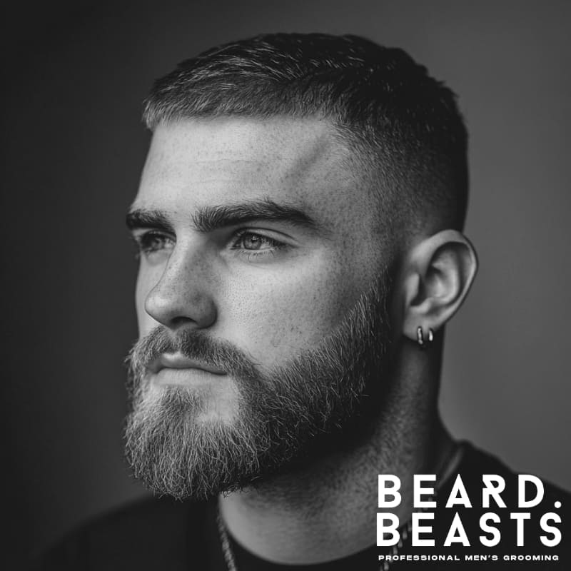 Black and white image of a man with a modern crew cut fade and full beard, showcasing a clean, structured hairstyle.