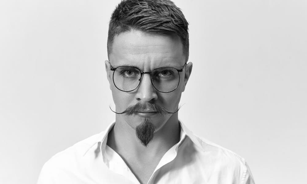 Man with an overly styled mustache and pointed goatee, showing a dramatic grooming look with curled tips.