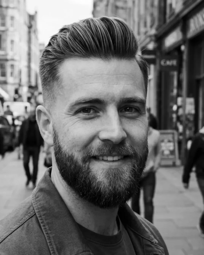 Short pompadour with a beard, showing lifted hair styled back with short sides and fuller facial hair.