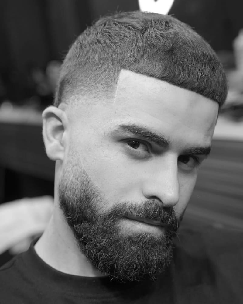Man with a taper fade crop haircut paired with a full beard, showcasing a sharp hairline and clean skin fade sides.