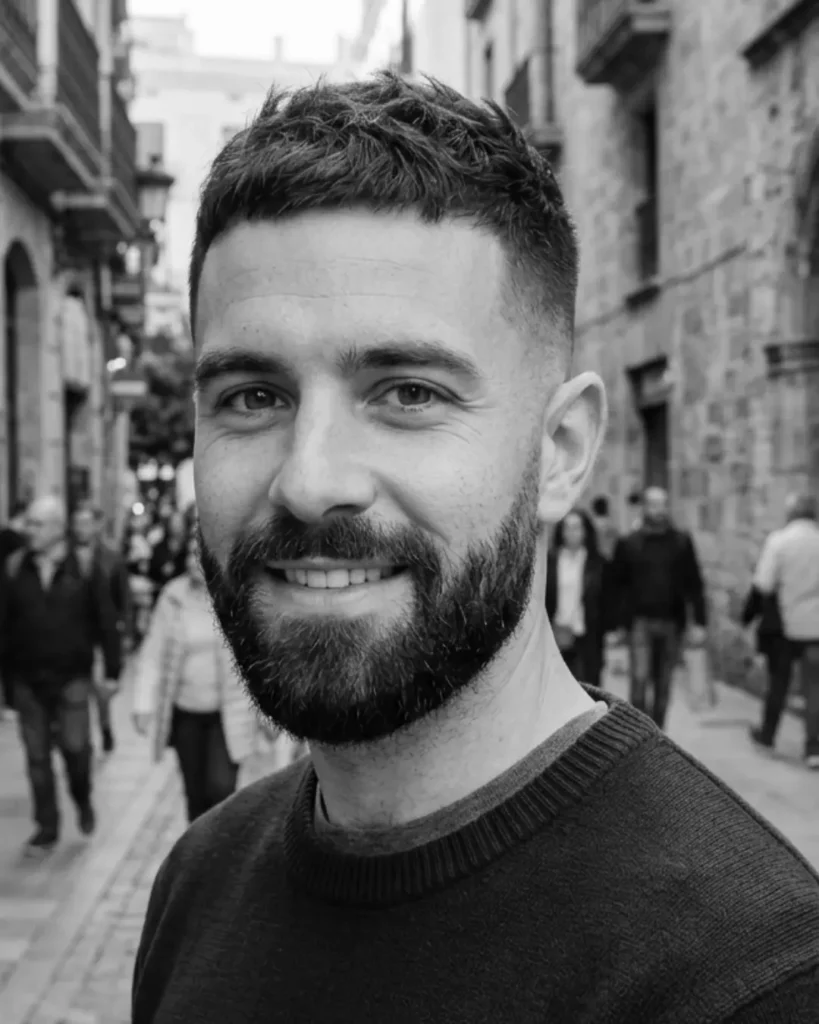 Taper fade crop with a beard, showing short textured hair with tapered sides and shaped facial hair.