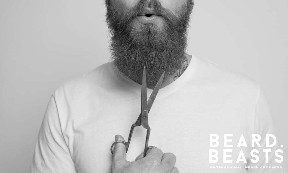 Close-up of a bearded man holding scissors near his beard, highlighting careful beard trimming as part of a smart grooming routine.