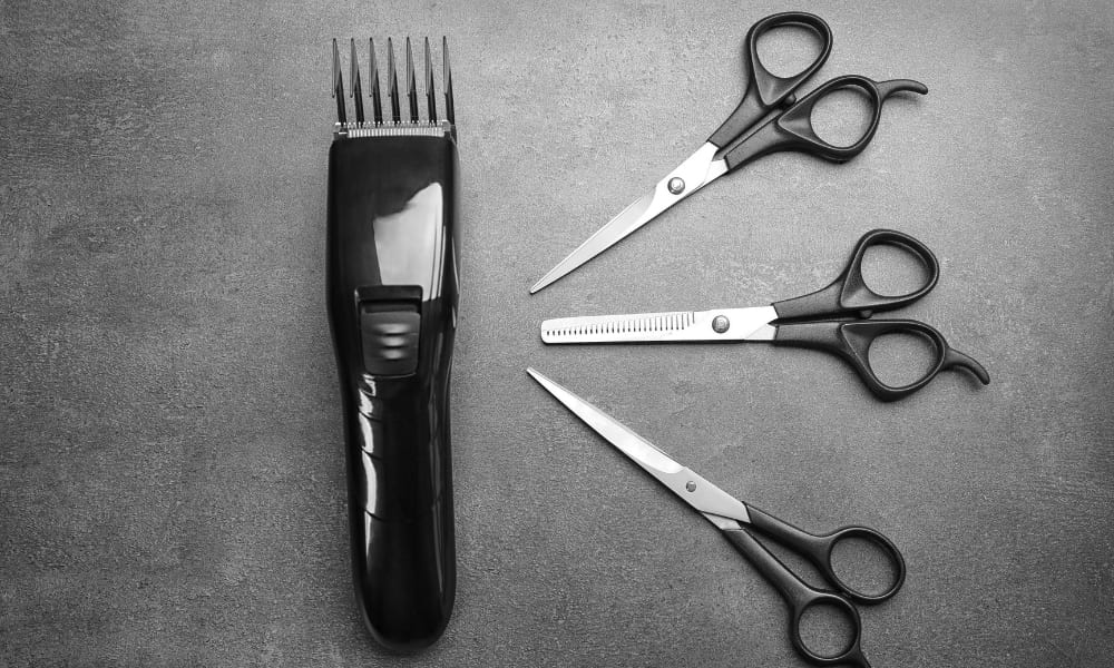 Flat lay of grooming tools including scissors, a comb, and an electric trimmer on a white background.