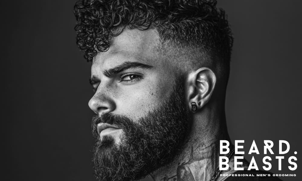 Black and white side portrait of a man with a curly beard and sharp fade, symbolizing an untamed, unruly beard before grooming.