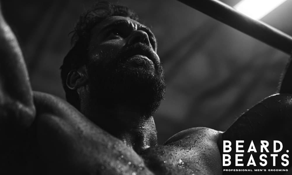 Low-angle shot of a muscular bearded man doing pull-ups, captured in moody lighting to convey power, focus, and endurance.