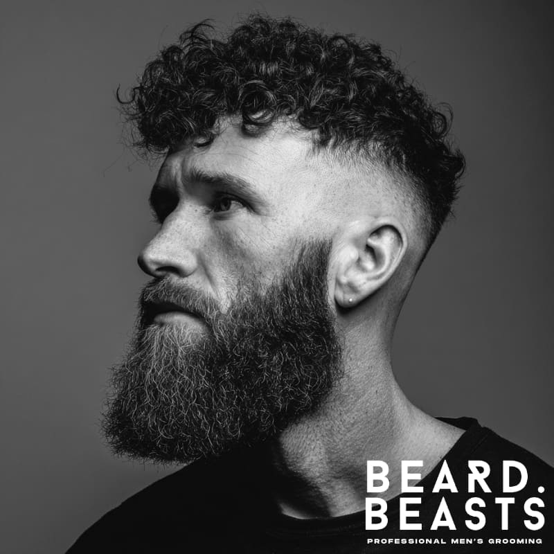 Man with a curly undercut and long beard, featuring defined curls on top and a full beard for strong contrast
