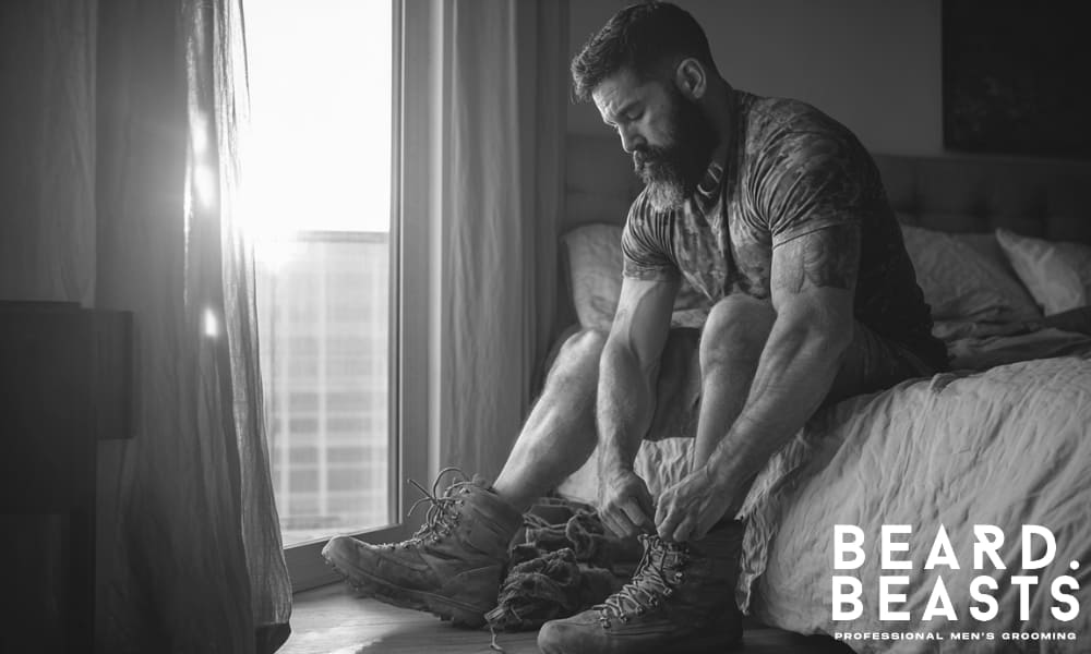 Bearded man lacing up boots at sunrise beside his bed, capturing a quiet moment of focus, routine, and early-morning discipline.