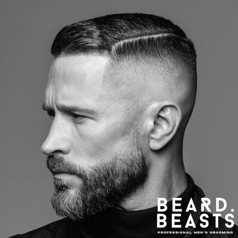 Man with a hard part undercut and short beard, featuring a defined part line and clean fade for a sharp, structured look