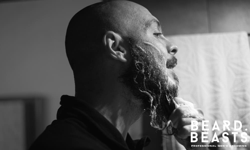 Man washing his beard with cleanser in a bathroom mirror—visual guide related to how often you should wash your beard for healthy grooming.