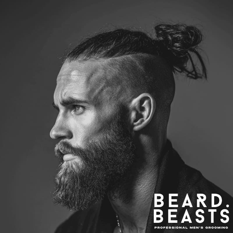 Profile shot of a man with a high undercut man bun and full beard, showcasing sharp grooming lines, textured hair, and a strong masculine look—ideal pairing for modern man bun and beard style.