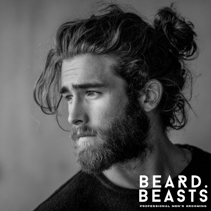 Black and white portrait of a man with a messy man bun and textured full beard, featuring loose, wavy strands and natural grooming—rugged yet refined with a relaxed finish.