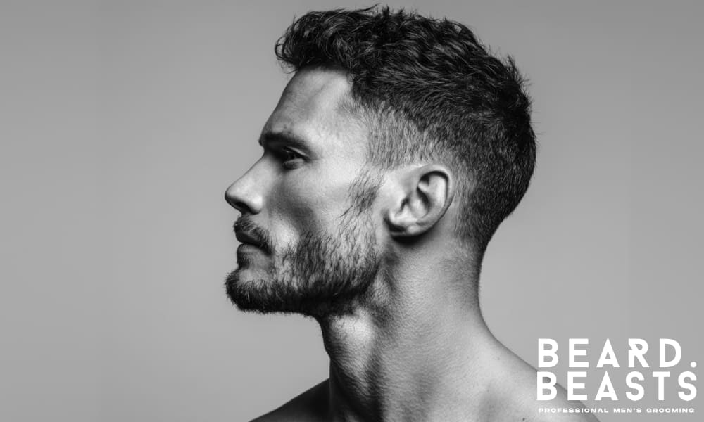 Side profile of a man with uneven facial hair and light cheek growth, illustrating a beard style that lacks definition and structure.