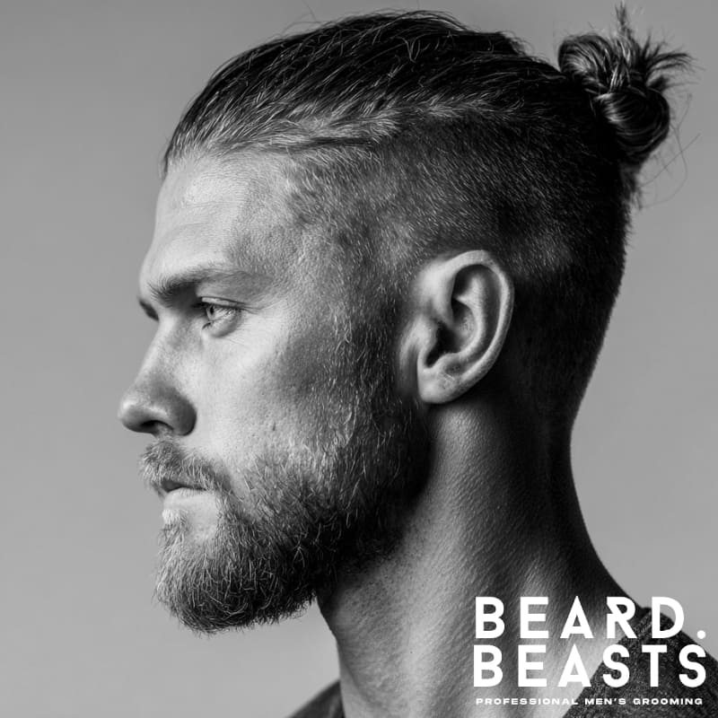 Black and white side profile of a man with a short man bun and a neatly trimmed full beard, featuring a tight fade and defined grooming—clean, minimal, and sharply styled.