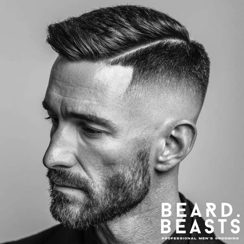 Man with a side-part undercut and short beard, featuring a clean fade and sharp part line—modern men’s grooming style.
