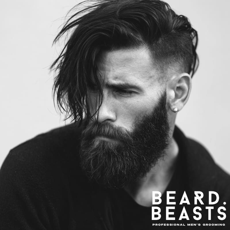 Man with a side-swept undercut and full beard, showcasing a bold, textured hairstyle with strong contrast
