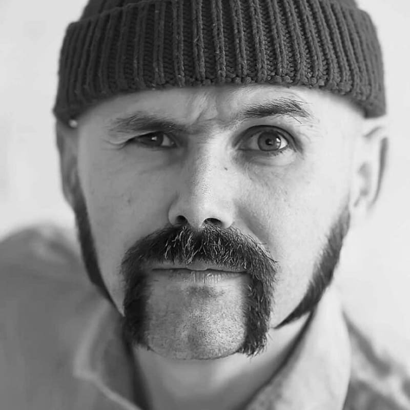 Man with a neatly trimmed horseshoe mustache and knit cap, showing a modern and refined take on the classic mustache style