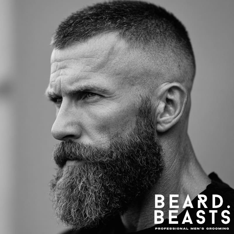 A man showcasing a crew cut fade hairstyle paired with a full, textured beard, creating a rugged and well-groomed look.