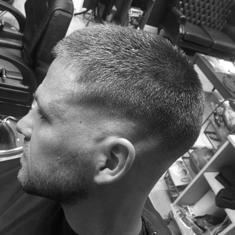 A man showcasing a crew cut low fade hairstyle, featuring a subtle fade starting just above the ear and a neat, short top.