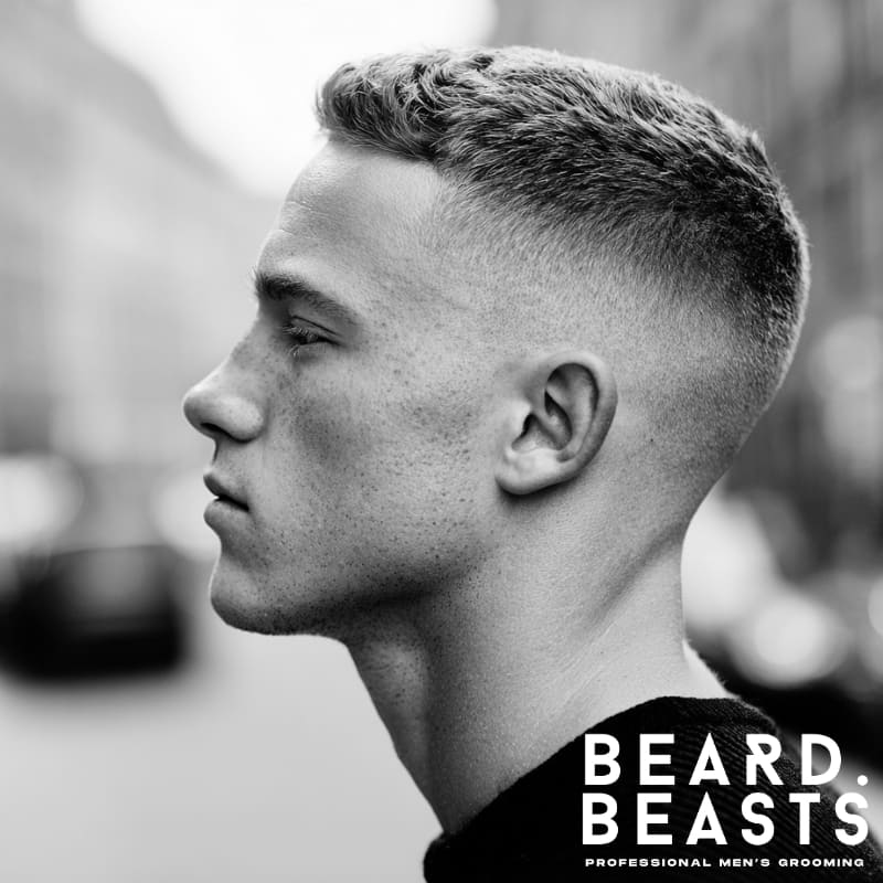 A man showcasing a high fade crew cut hairstyle, characterized by an aggressive, high-contrast fade on the sides and a textured, longer top.