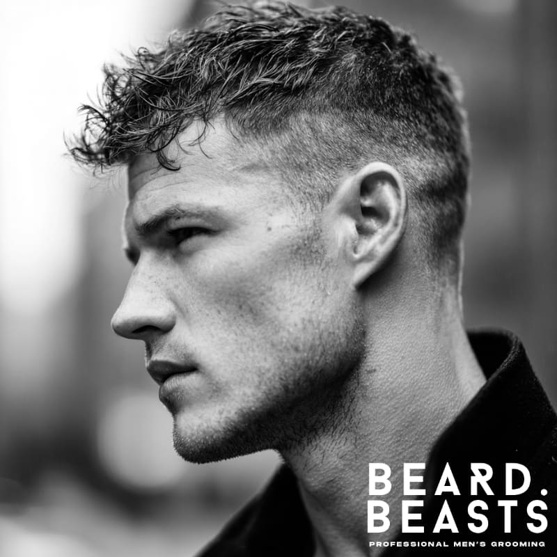 A man sporting a messy crew cut hairstyle, featuring a textured, disheveled top with natural waves and clean, faded sides.