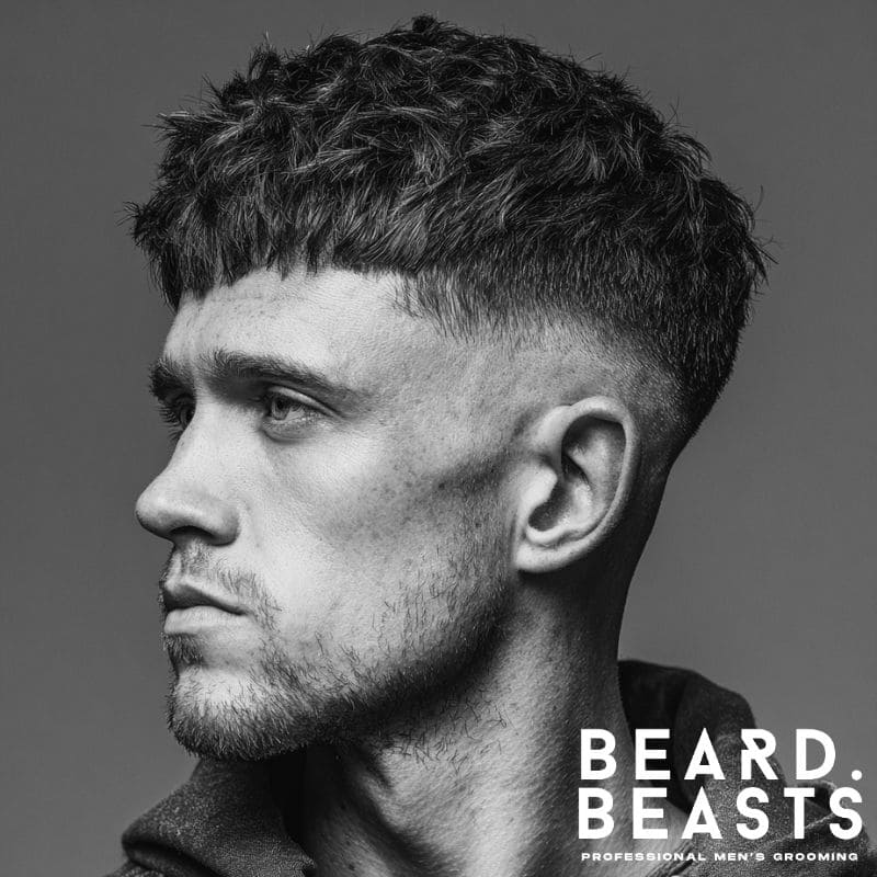 Side profile of a man with a mid skin fade and textured fringe haircut, showcasing natural volume and defined edges.