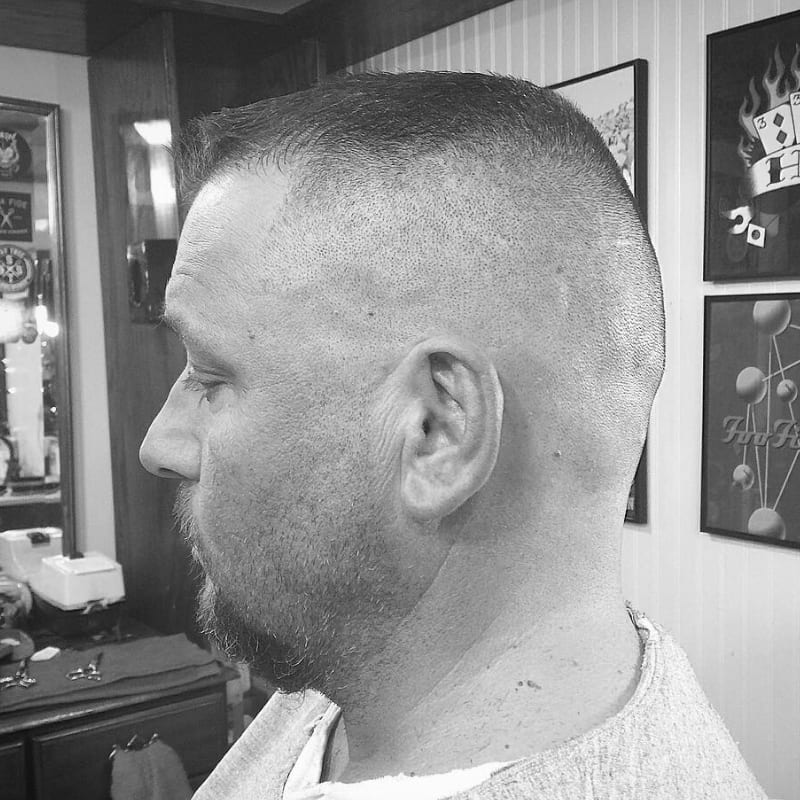 A man showcasing a military-inspired crew cut hairstyle, featuring an ultra-short, precisely cropped top and an aggressive taper on the sides.