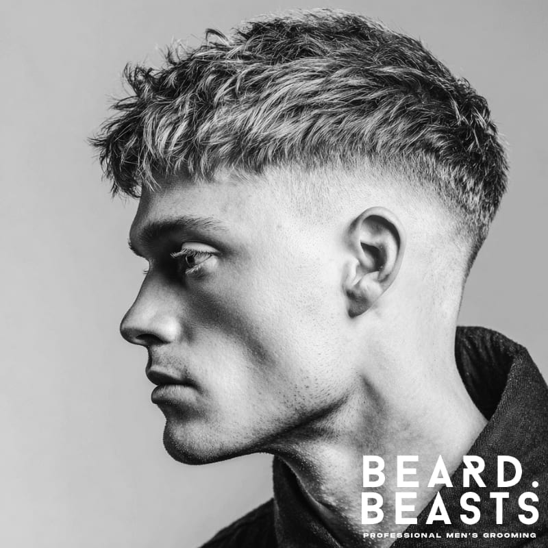 Side profile black and white portrait of a man showcasing a trendy short textured fringe with a clean drop fade haircut.