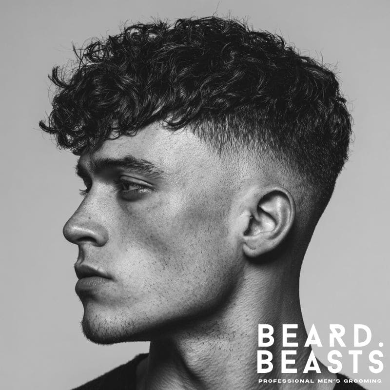 Side profile of a man with a curly skin fade and textured fringe, showcasing defined curls and a sharp fade.