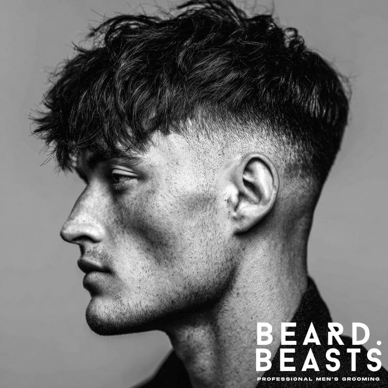 Side profile of a man with a skin fade and long textured fringe haircut, showcasing natural volume and defined texture.