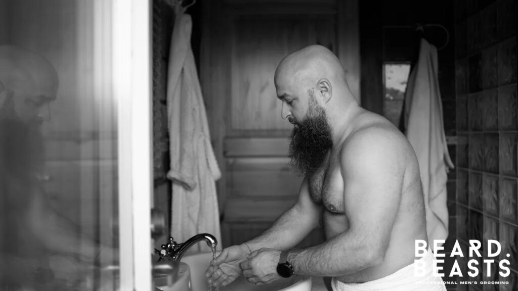 Man with a full beard preparing to exfoliate at the sink, showing the first steps of how to exfoliate your beard properly.