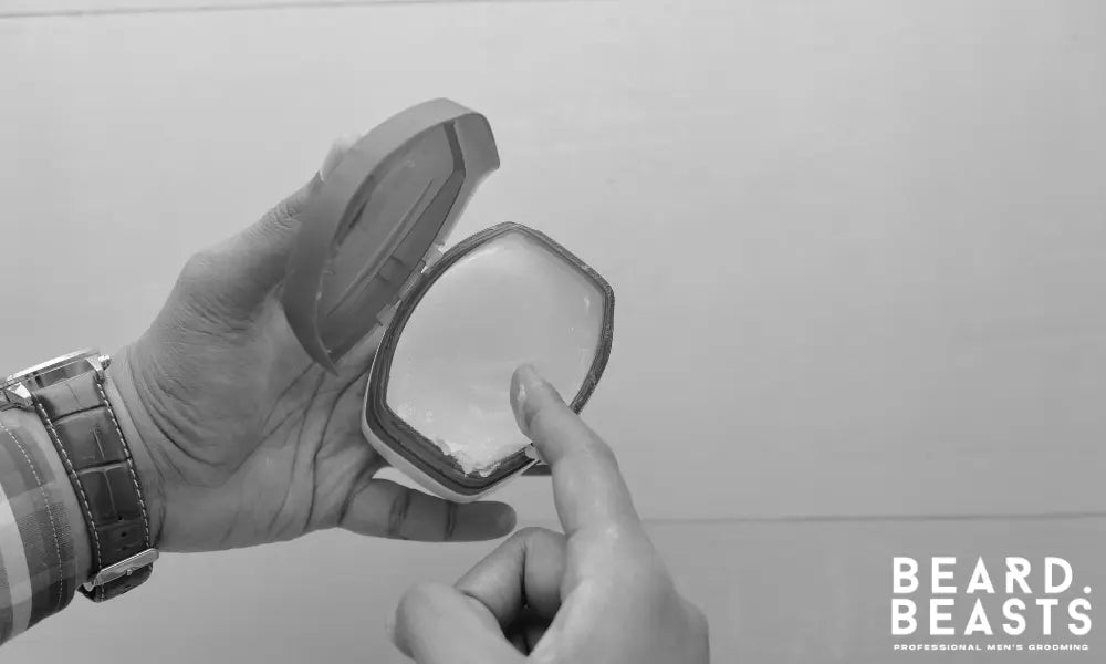 Man dipping a finger into Vaseline petroleum jelly, often questioned for beard use but not recommended for healthy facial hair care.