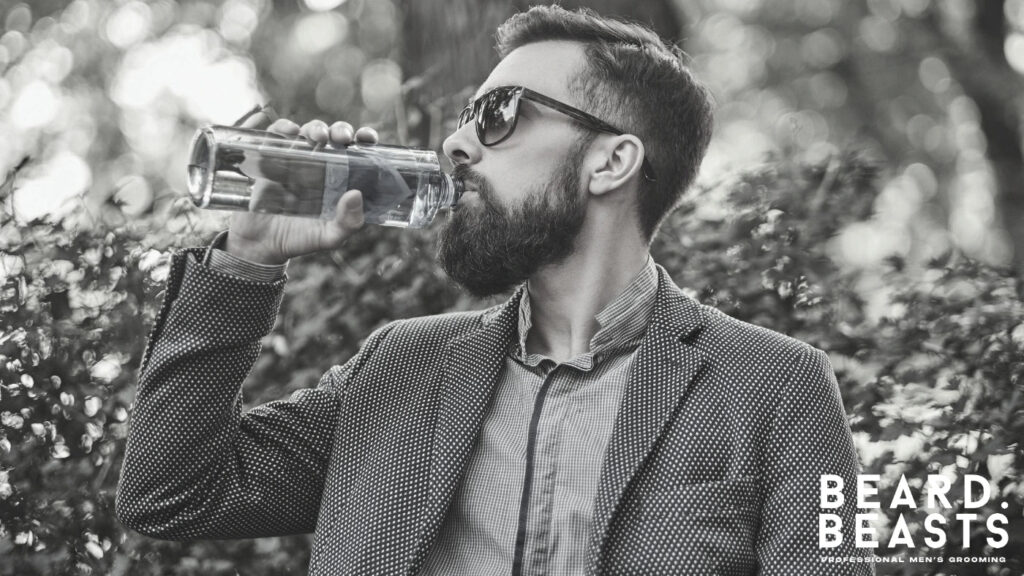 Bearded man drinking water outdoors, representing hydration and healthy habits that keep beard hair soft and reduce roughness.
