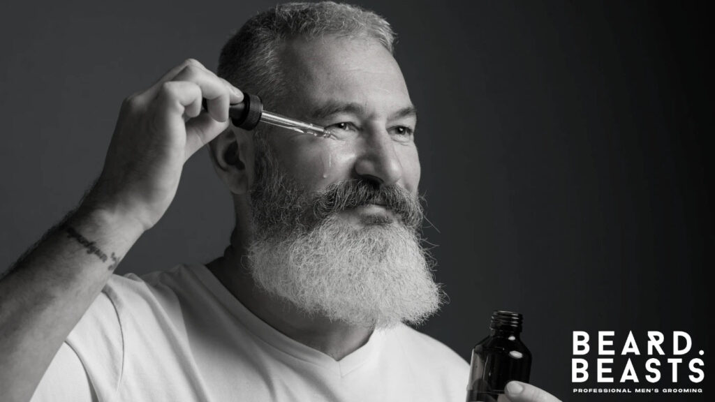 Older man with a full white beard applying beard oil to his face to show the benefits of proper beard care