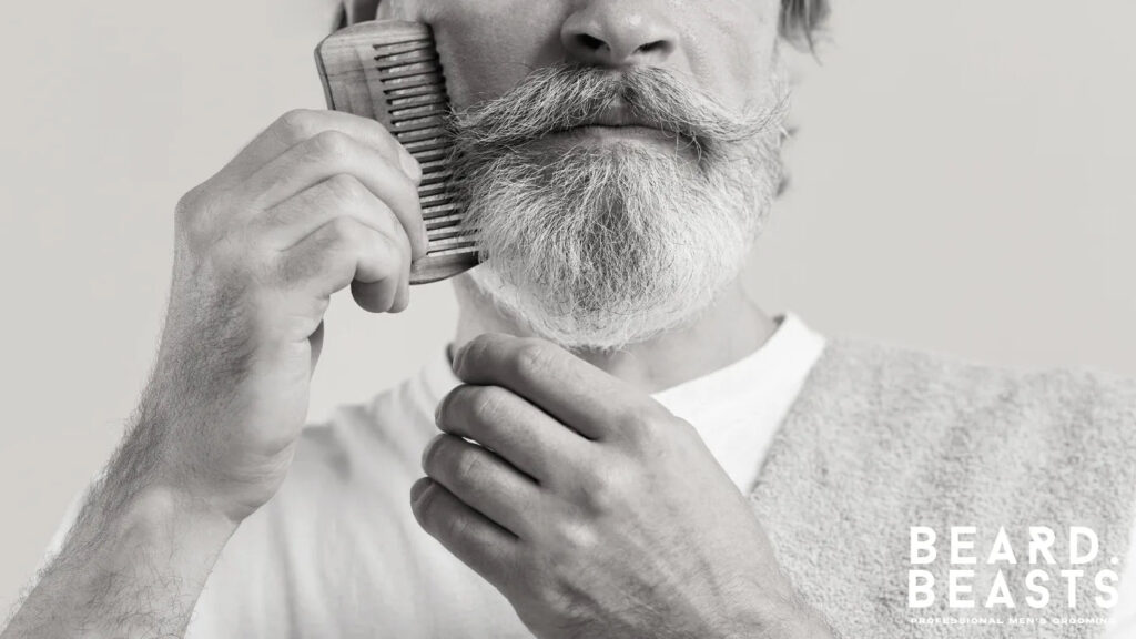 Older man combing his beard with a wooden comb to straighten and detangle before trimming