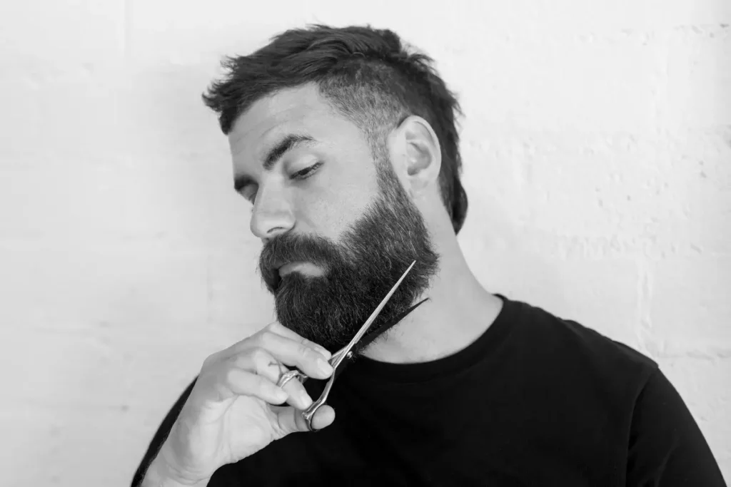 Man trimming a full beard with scissors for a sharper beard shape