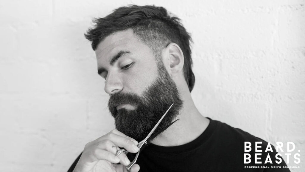 Man carefully trimming his beard with scissors to refine edges and remove stray hairs