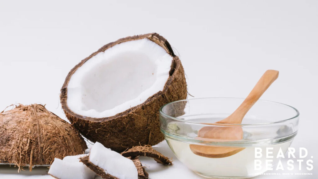 Glass bowl of coconut oil with fresh coconut halves and pieces, a nourishing carrier oil for dry and brittle beards.