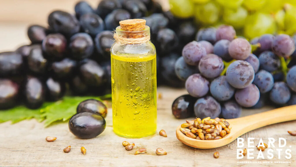 Glass bottle of grapeseed oil with fresh grapes and seeds on a wooden table, a lightweight carrier oil for beard hydration and oily skin.
