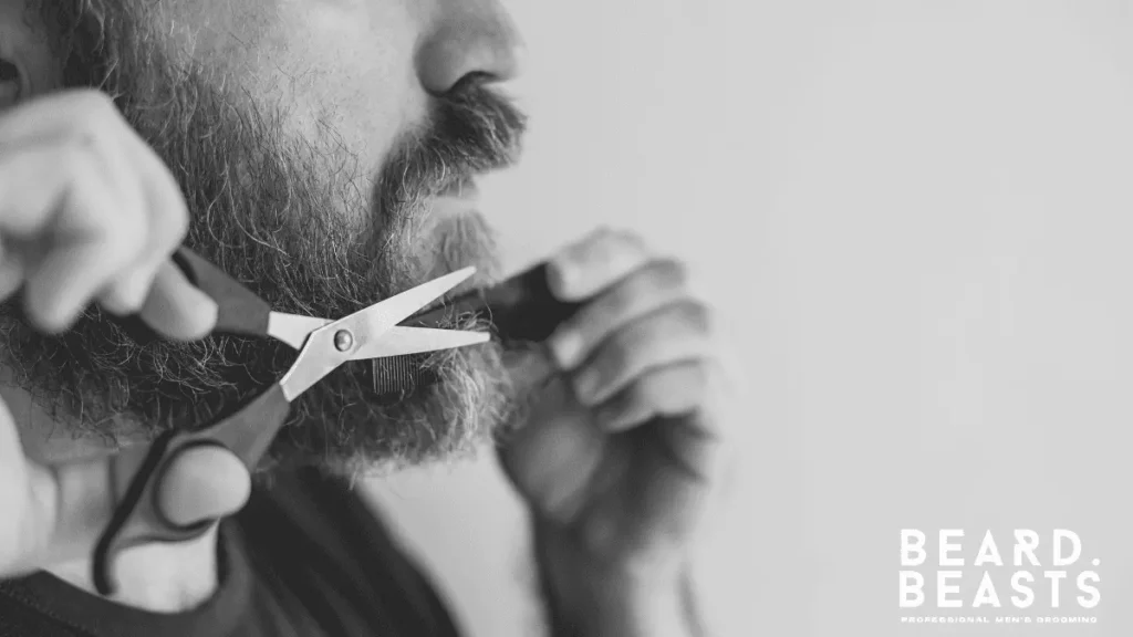Man trimming his beard with scissors at home, maintaining beard shape to balance a heart-shaped face and strengthen the jawline.